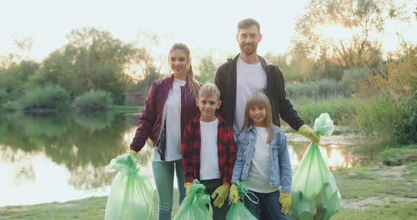 Family Posing on Camera with Plastic Rubbish Bags After Cleanup Surrounding Territory Near Lake