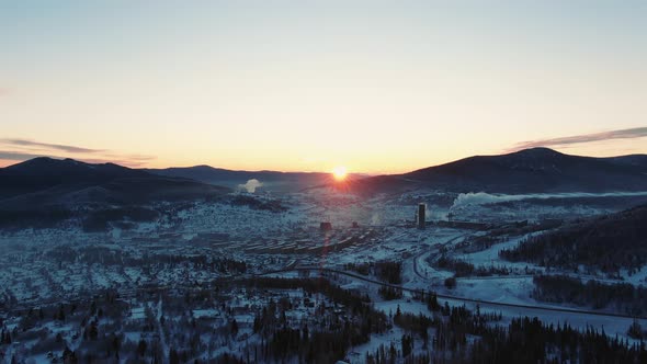 Town and Plant with Chimney in Snowy Valley Near Mountains