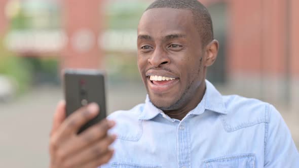 Outdoor Portrait of Excited African Man Celebrating on Smartphone 