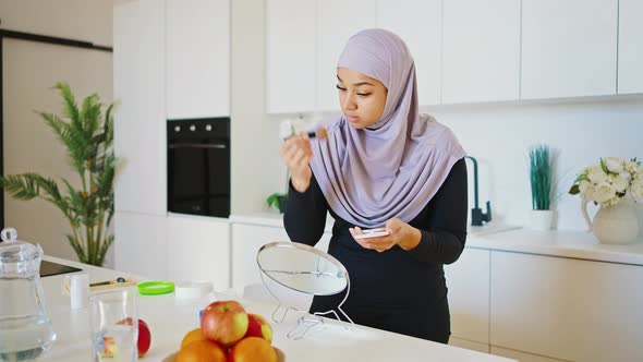 Young Modern Woman in Hijab Doing Makeup in Front of the Mirror While Sitting in the Kitchen