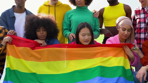 Group of multiracial people having fun at city park with rainbow flag - LGBT gay pride event