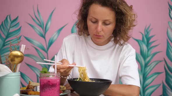 Young Caucasian Woman Eating Vegan Ramen Soup in Trendy Colorful Cafe