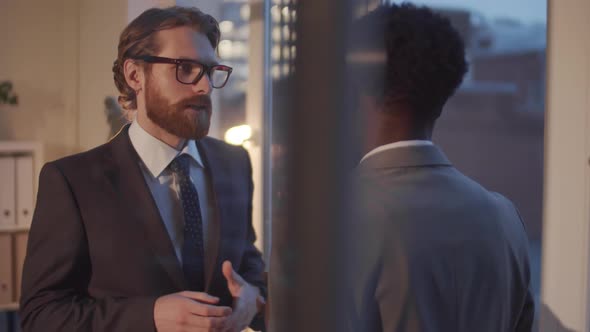 Two Multiethnic Businessmen Speaking in Office in the Evening