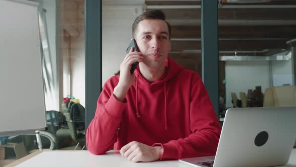 Portrait of Young Man Talking on Mobile Phone While Sitting at Workplace at Office