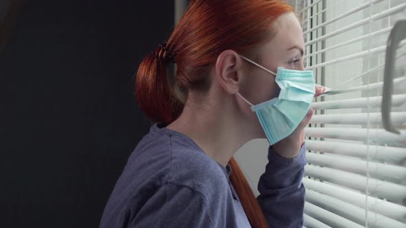 A Woman in a Protective Mask Looks Out the Window.