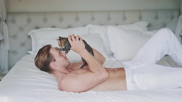 Sporty Caucasian Man Plays with Nice Little Kitten on Bed