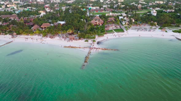 Aerial shot approaching to a group of people on a cross-shaped breakwater. Turquoise beach and sea o