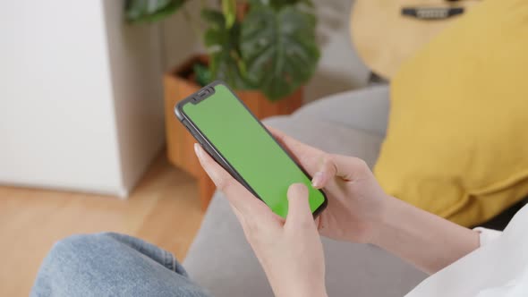 Woman holding mockup smartphone green screen on the sofa at home.