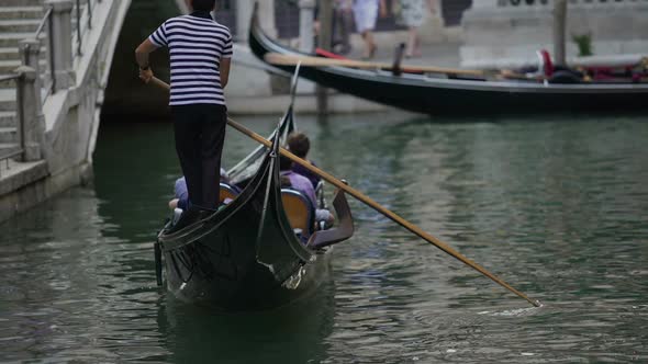 Male Gondolier Riding Curious Tourists on Canal, Showing Attractions of Venice