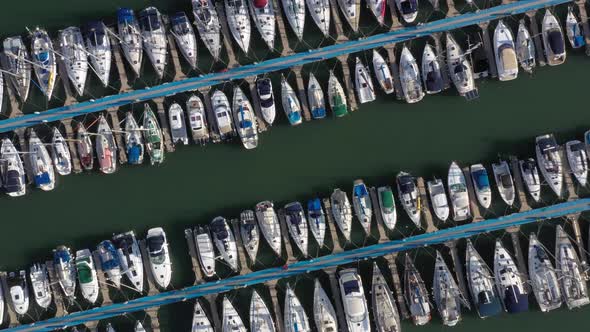 Several sailing yachts with folded sails are quietly moored to the long blue jetties in the Herzeliy