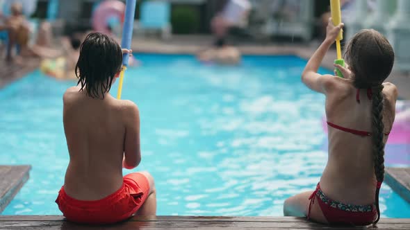 Back View Carefree Children Sitting on Pool Deck Playing with Water Gun