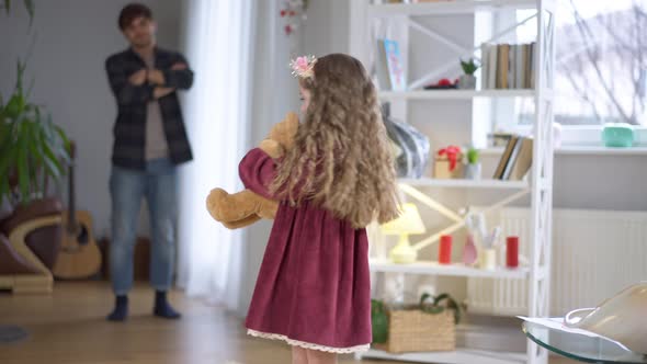 Sad Pretty Girl Looking Back at Blurred Man with Crossed Hands and Looking at Camera Hugging Teddy