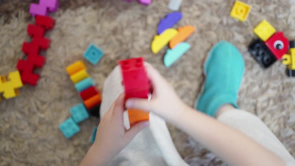 Children's Hands Play on a Soft Carpet with Different Colored Details of a Plastic Constructor