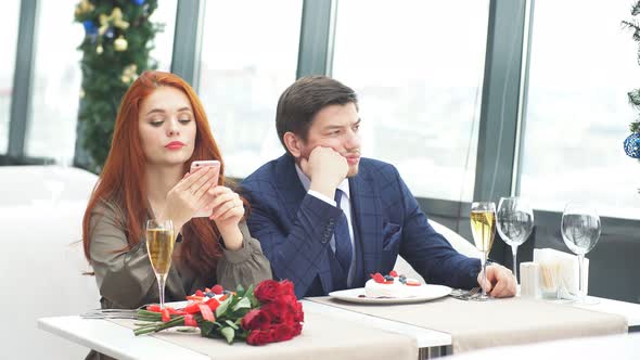 Young Caucasian Man in Tuxedo and Redhaired Woman in Dress Sit Bored in a Restaurant.