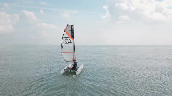 Man sailing his catamaran in the sea. Drone follows behind, beautiful coastal landscape.