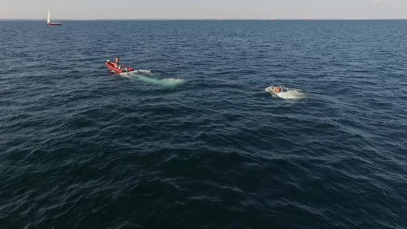 Man Standing on Red Inflatable Boat with Motor Pulling with Rope Another Male in Sea in Slowmotion