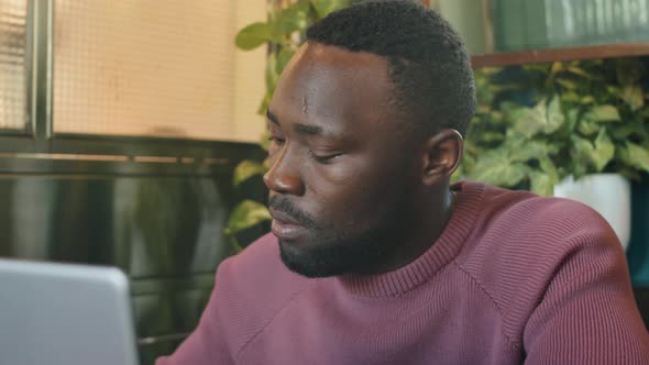 Black Man Working on Laptop and Taking Notes in Cafe