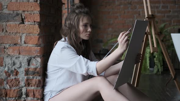 Girl Artist Paints a Picture in the Home Studio. Portrait of the Painter in the Loft.