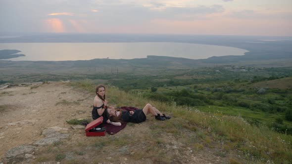 Two Hipster Girls Lie on the Ground in the Mountains and Listen To Music