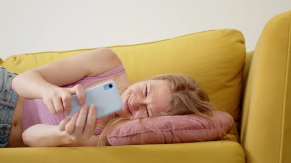 Happy and Cheerful Woman in Pink Tank Top Follow Shot Lies Down on Pillow on Yellow Sofa with Happy