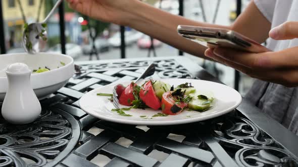 Woman Puts Vegetable Salad in a Plate and Uses the Phone at Dinner in a Restaurant