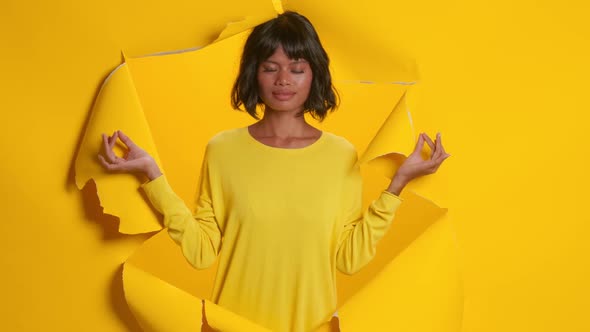 Peaceful Dark Skinned Young Woman Meditates and Holds Zen on Yellow Background
