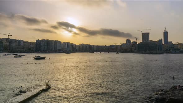 View of skyline of resort town Sliema at sunset, people swimming, Malta, time lapse