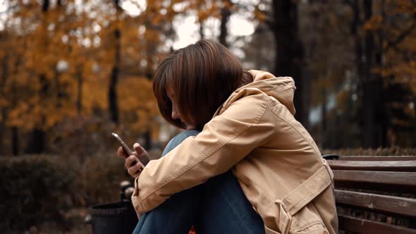 Young Girl Sitting Alone in a Park with a Phone