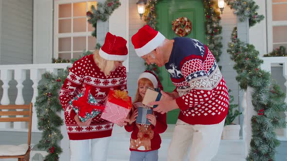 Senior Grandparents with Grandchild Girl Kid Exhcanging Gifts Near Christmas House Celebrating Xmas