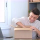 Smiling man wearing glasses unpacking awaited parcel, looking inside, sitting at work desk - VideoHive Item for Sale