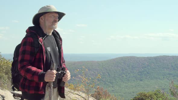 An older hiker looking through binoculars while on a scenic hike in the mountains