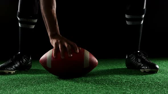 American football player bending holding a ball on turf with his hands 4k