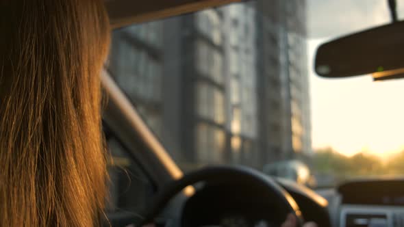 Rear view of female driver behind steering wheel driving a car on a city street.