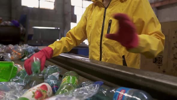 Unrecognizable Person in Yellow Jacket and Gloves Sorting Used Plastic Bottles at Recycling Plant