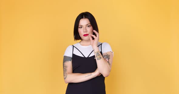 Smiling hipster woman with tattoo keep secret and looking at the camera on yellow background. 