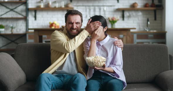 Young People Watching Horror Movie on TV with Popcorn Sitting on Couch in Apartment