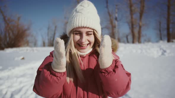 Beautiful Woman in White Knitted Hat and Red Winter Jacket Throws Up Snow