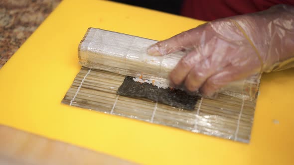 Hands in Gloves Making a Sushi Roll with Eel and Shrimp