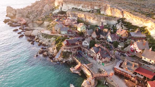 Rocky cliff side coastal wooden town in Malta island, aerial view during golden sunset