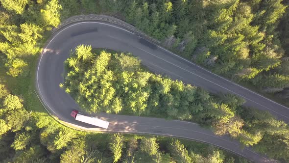 Aerial view of winding road with mowing cars and trucks in high mountain pass trough dense woods.