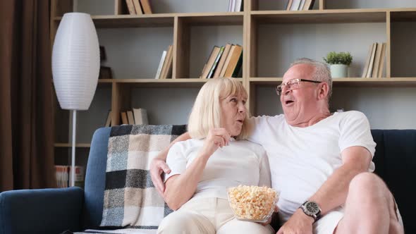 Happy Elderly Married Couple Watching Tv Sitting on Sofa Old Couple Eating Popcorn and Laughing