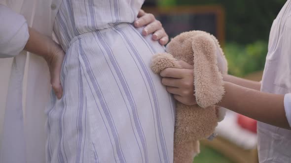 Closeup Side View Teenage Hands Hugging Pregnant Belly with Toy in Slow Motion Outdoors