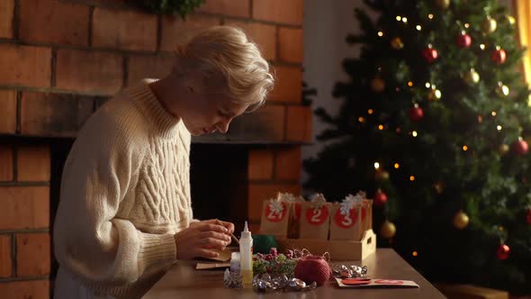 Side View of Happy Young Woman Making Paper Bags From Kraft Paper for Advent Calendar on Christmas