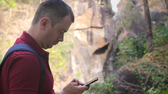 Worried Man with Backpack in National Park Looking at Map on Cell Phone