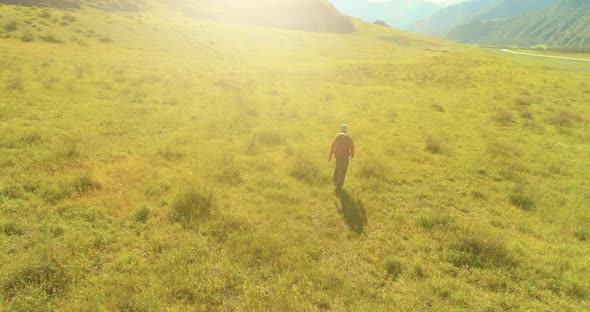 Flight Over Backpack Hiking Tourist Walking Across Green Mountain Field. Huge Rural Valley at Summer