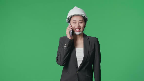 Asian Female Engineer With Safety Helmet Talking On Smartphone And Walking On Green Screen Studio