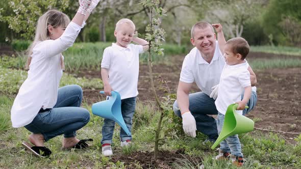 Parents and Two Little Sons Planting Tree in Village