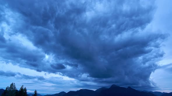 A huge storm cloud forms over the mountains at dusk. Twilight transition to night.