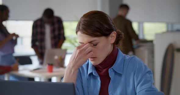 Frustrated Young Woman Keeping Eyes Closed and Massaging Nose Sitting at Working Place in Office