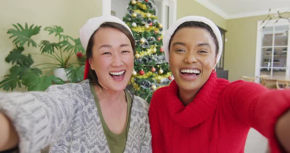 Happy diverse female friends in santa hats making christmas video call, blowing kisses and smiling